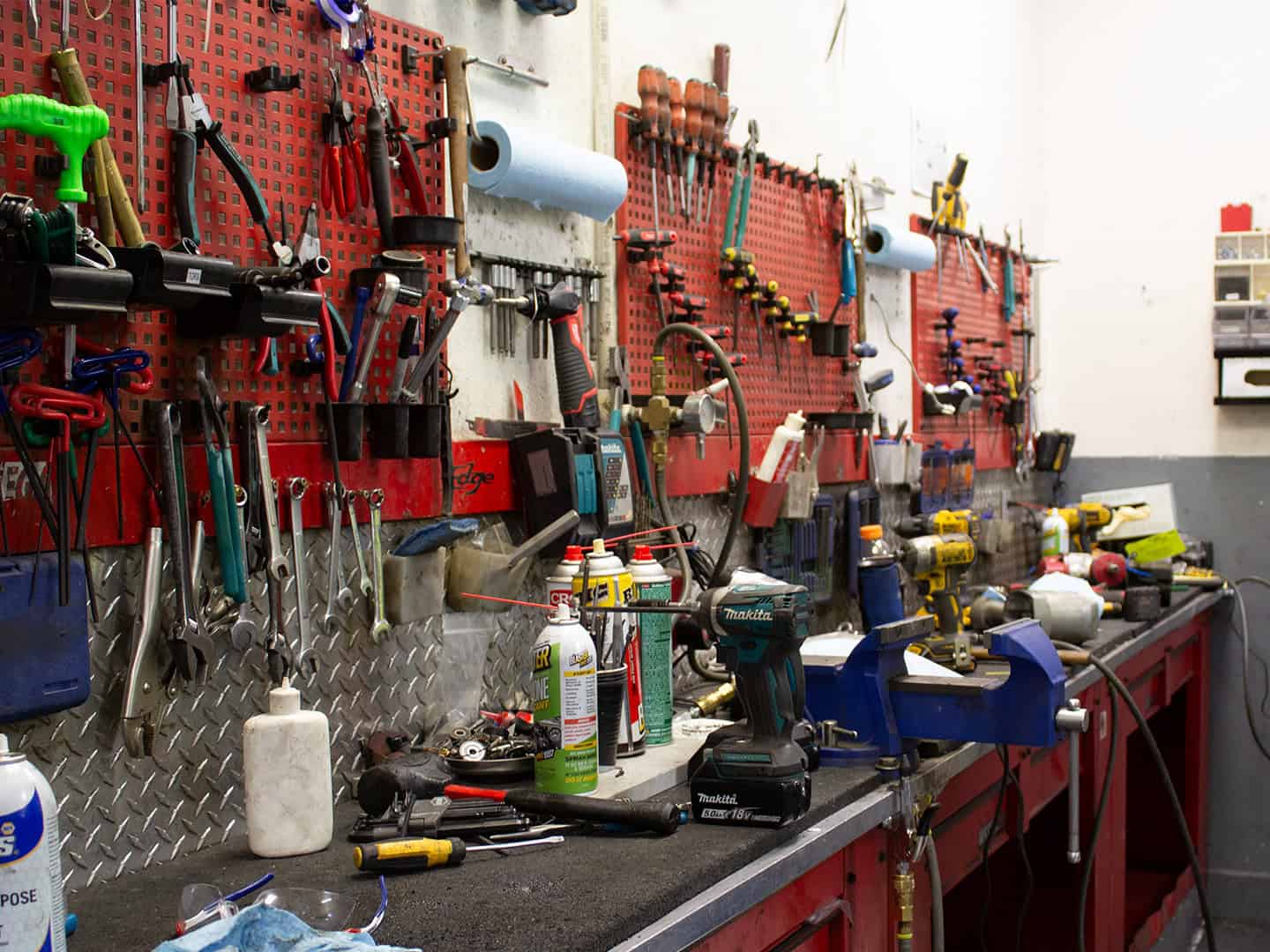 A cluttered workshop with various tools hanging on perforated boards and workbenches covered with equipment and supplies.