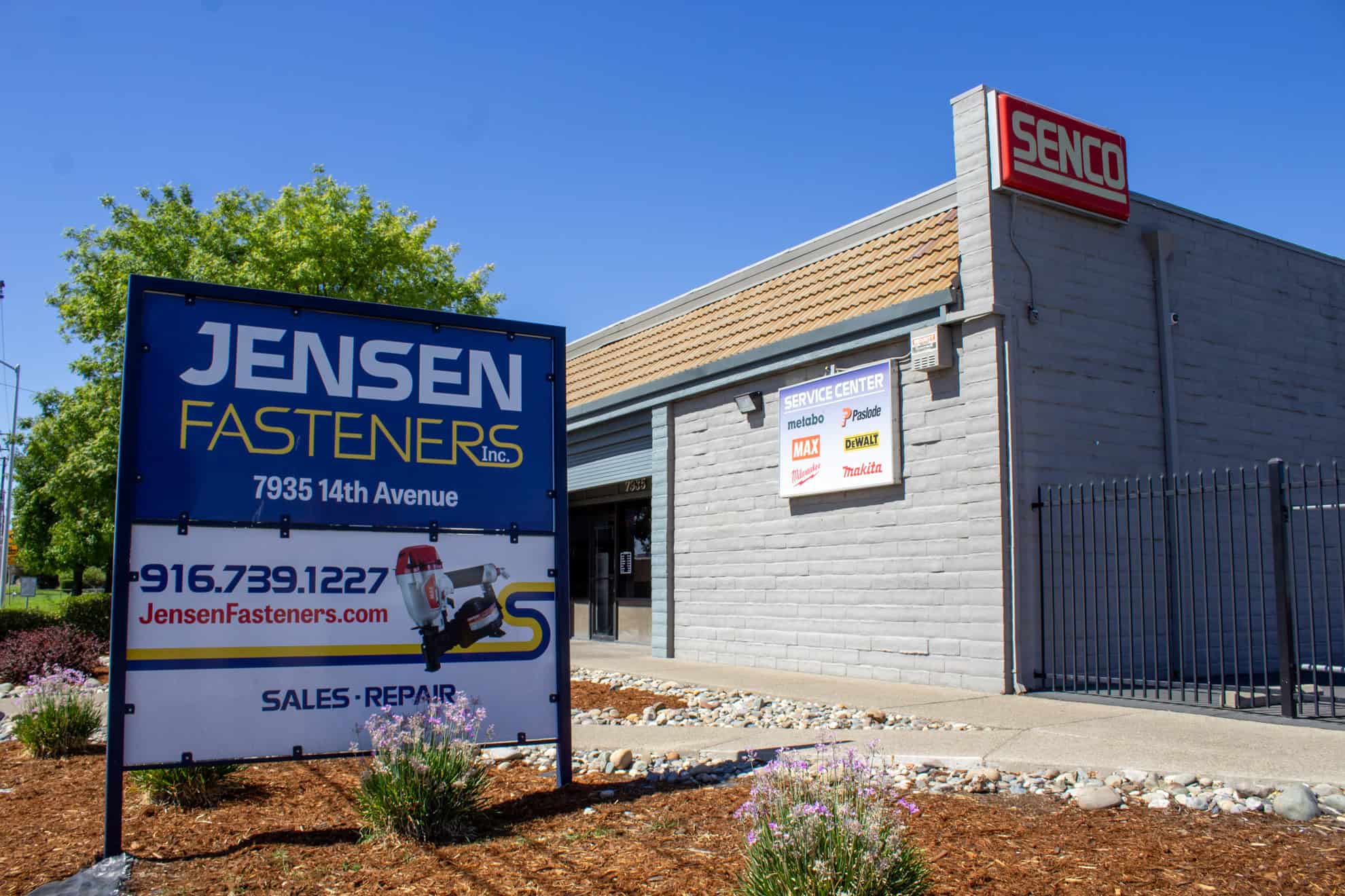 Sign for Jensen Fasteners Inc. outside a grey building with "Senco" on the wall. The location and contact number are displayed.