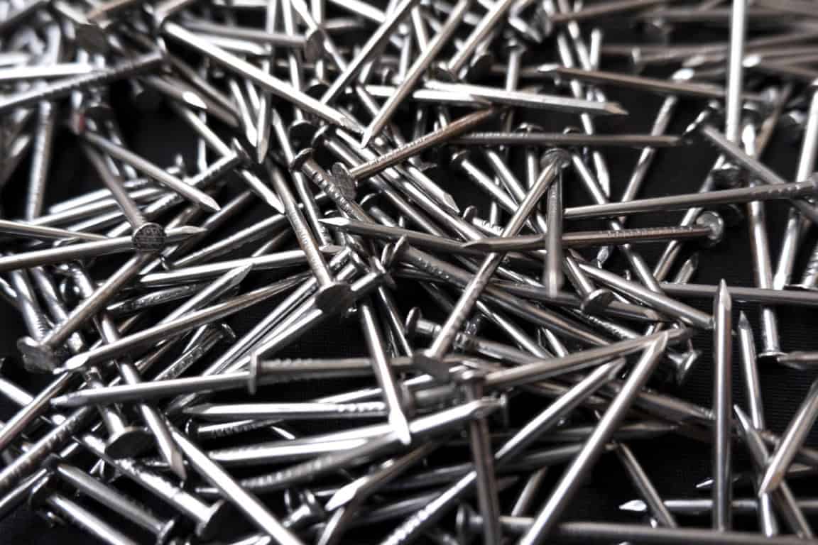 A pile of shiny metal nails scattered on a black surface.